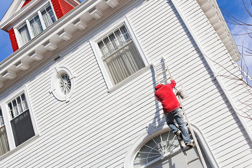 person climbing a ladder against a home exterior with paint can